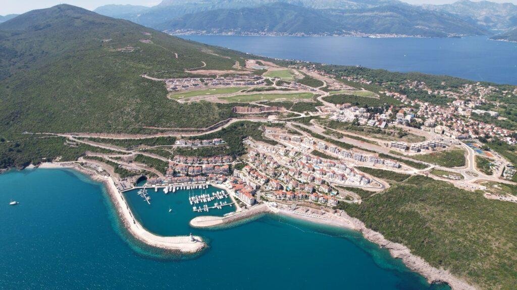 Dron snimak prikazuje citavu povrsinu koju obuhvata Lustica Bay i prikazuje okolinu koja ukljucuje naselje Radovici, zelenilo i more.