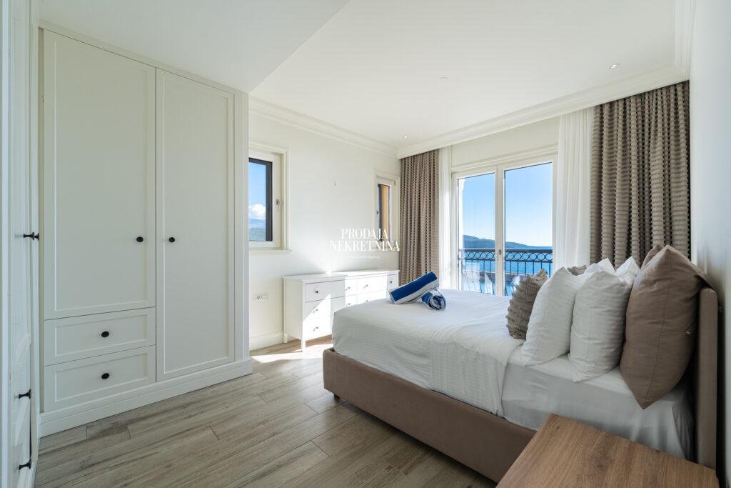 Seaview bedroom of a two-bedroom apartment in Lustica Bay. you can see the sea from the bed. Bedroom is minimalistic and white.