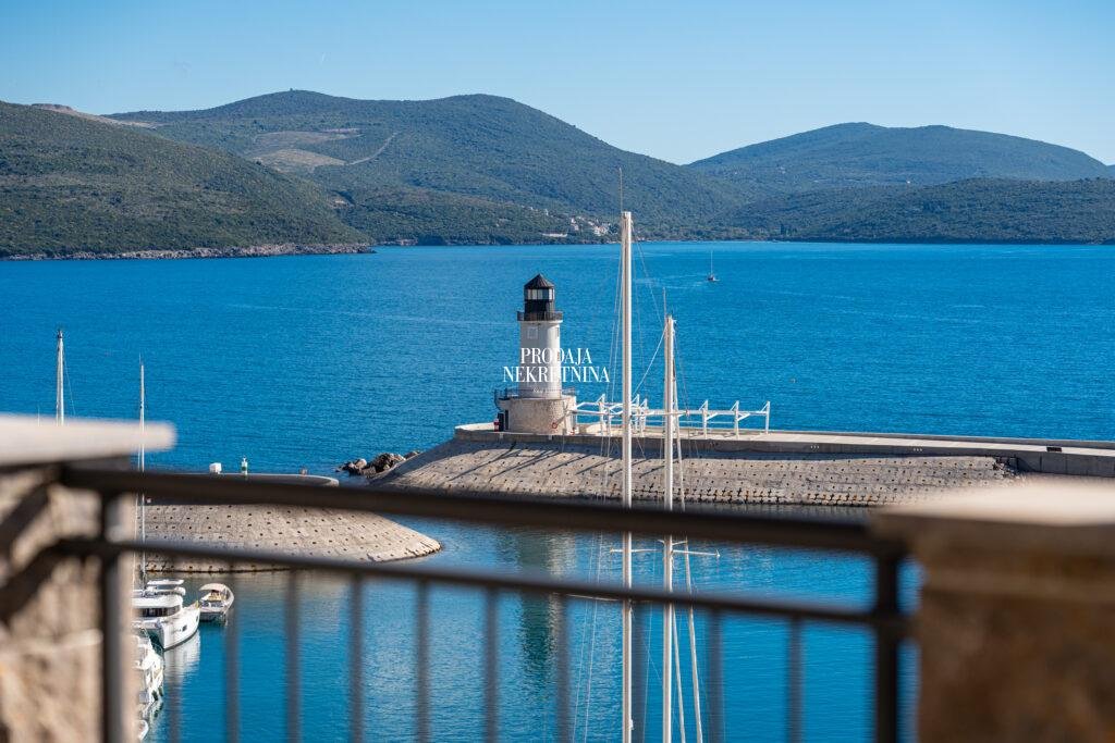 Pogled sa terase stana na more i svetionik u Marina Village, Luštica Bay. Vidi se deo ograde, more, svetionik i iza zelena brda sa netaknutom prirodom