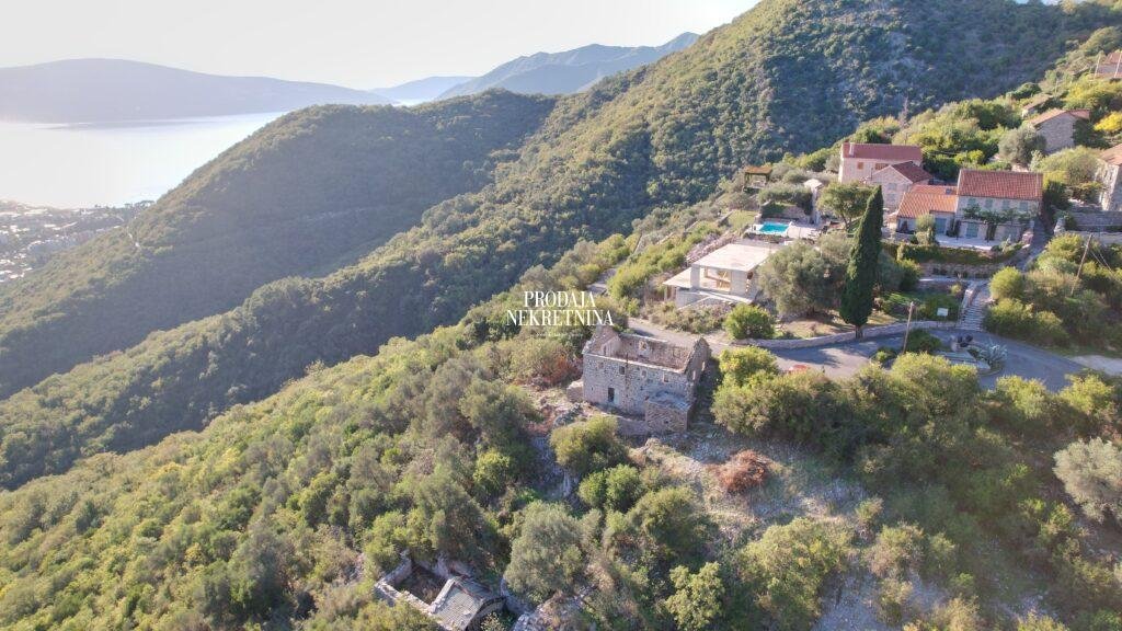 dron snimak zemlje u gornjoj lastci gde je prikazana kamena rusevina i nepregledno zelenilo koje vodi skroz do mora koje je u daljini. vidi se par okolnih objekata koji su zavrseni.