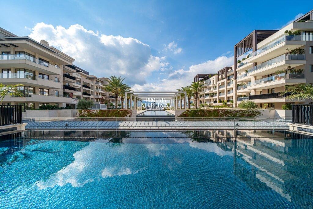 An infinity pool in Porto Montenegro, surrounded by buildings and landscaped greenery, with the sea and yachts visible at the far end of the pool.