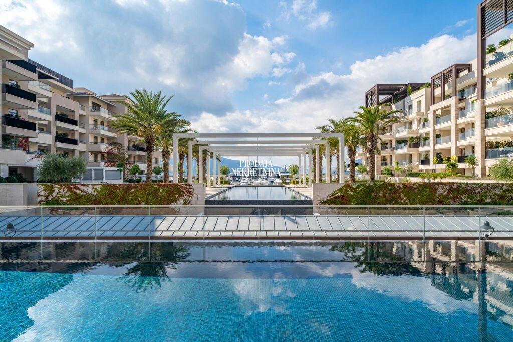 bazen u porto montenegru. infinity pool, sa strane su zgrade, uredjeno zelenilo, a na kraju bazena se nazire more i jahte